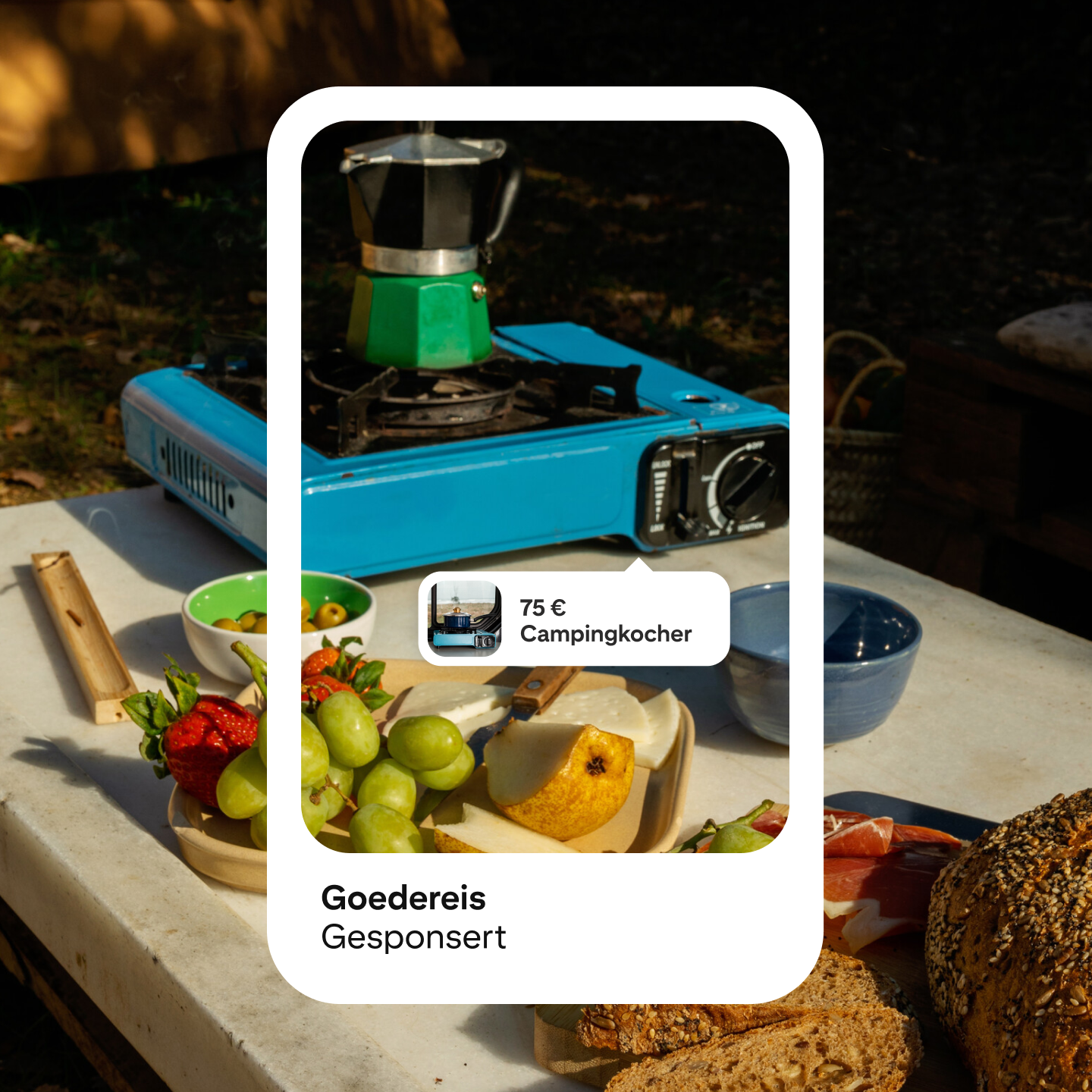 Bild eines Pinterest-Anzeigen-Mockup mit tragbarem Campingkocher in Blau und Silber. Der Preis liegt bei 75 £, der Text sagt „Campingkocher“, und die Anzeige ist von „Goedereis“. Draußen sind Früchte und Lebensmittel um den Kocher herum zu sehen.