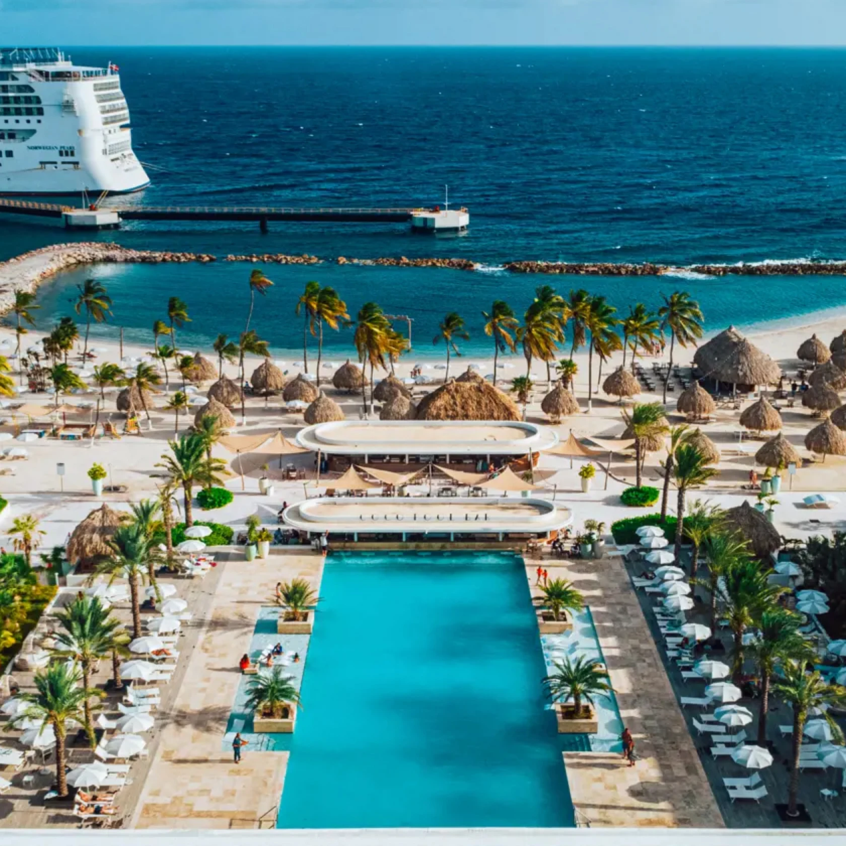 View of a resort pool overlooking the ocean and a cruise ship in the distance 