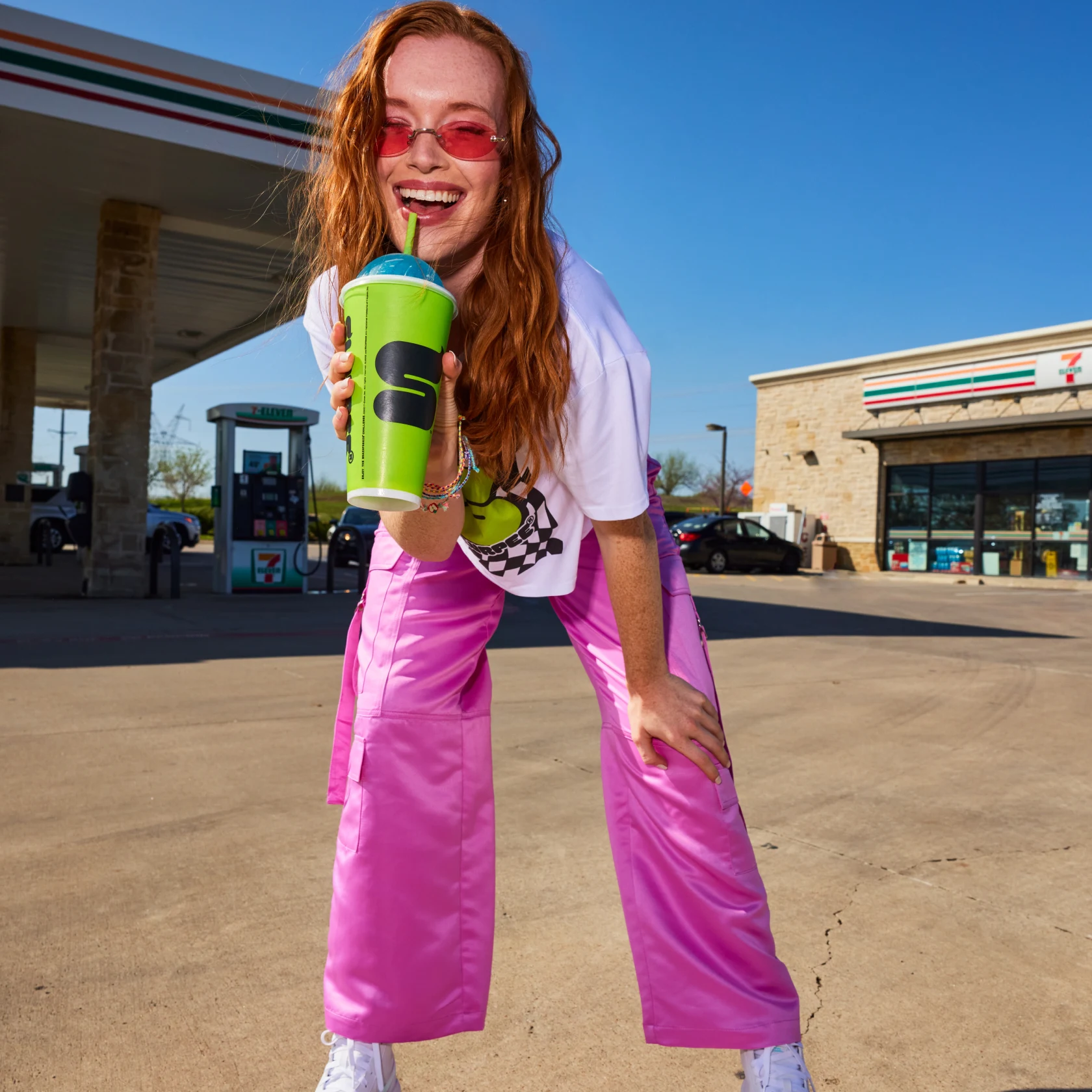 Girl stands outside of a gas station drinking a slurpee 