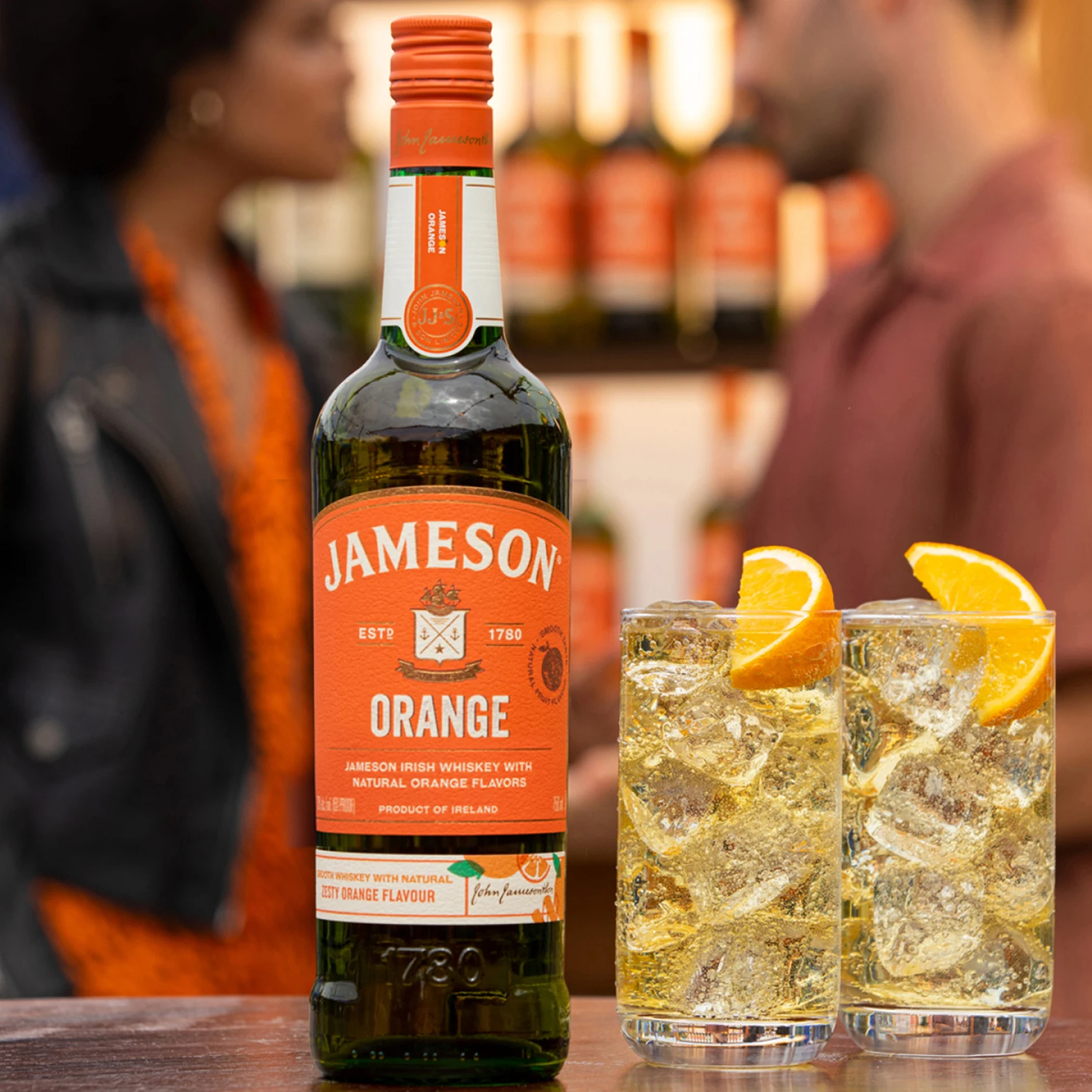 Bottle of Jameson orange sits alongside two cocktails glasses with ice and an orange wedge 