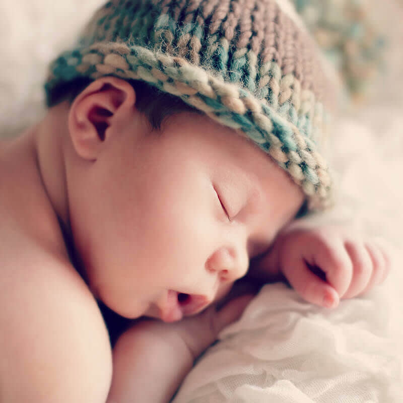 Sleeping newborn with woven cap on head.