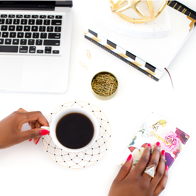 Flat lay of Black hands, laptop, mouse, coffee, paperclips, and notebook.