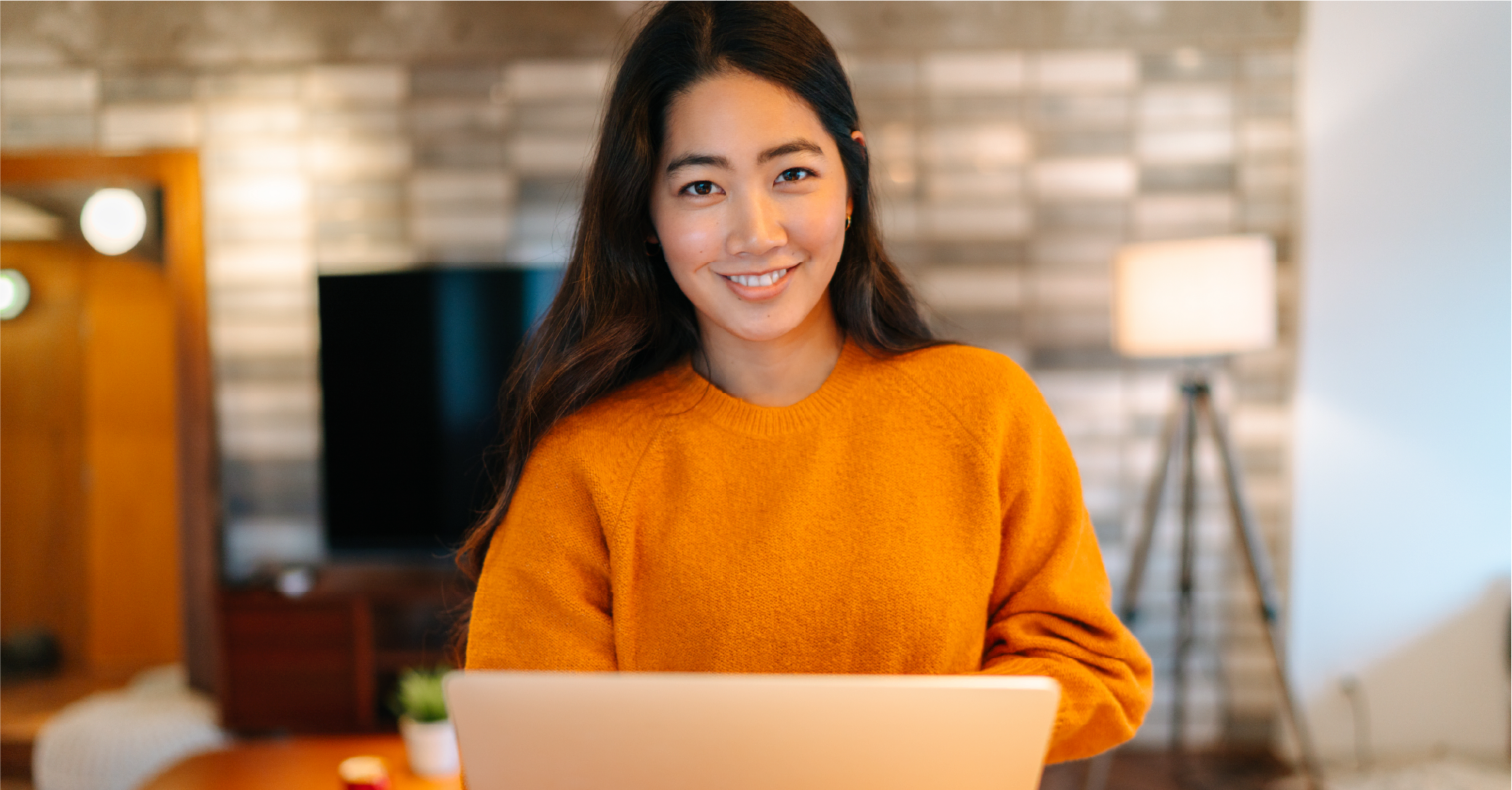 Smiling Lady in an orange knit jumper holding a laptop.
