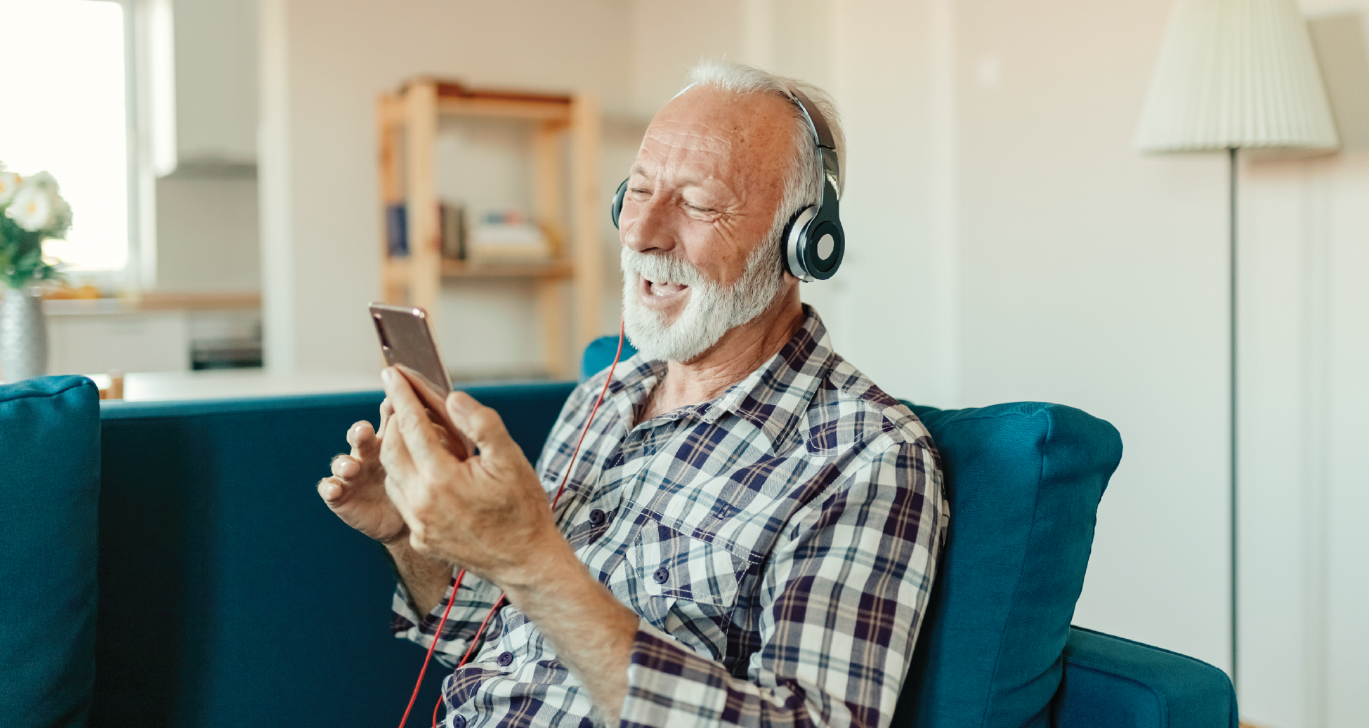 A old man with headphones on smiling at his phone.