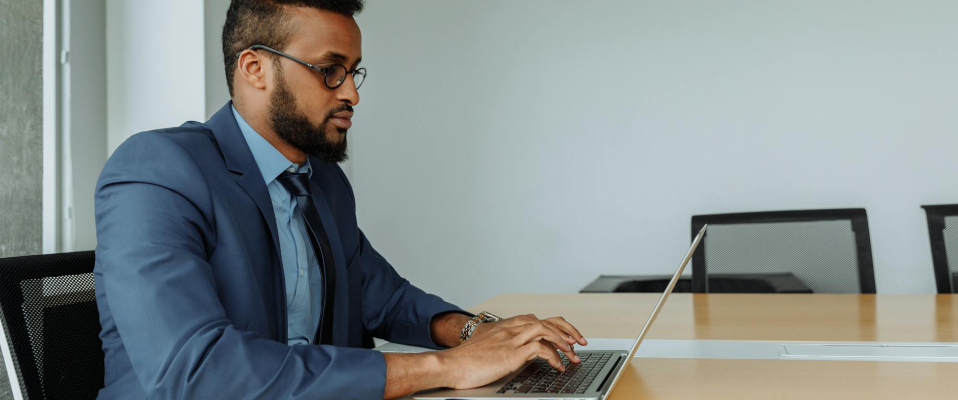 A man at a suit sits at a desk and types on a laptop