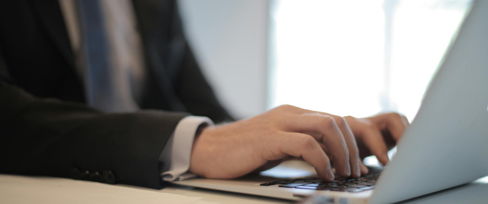 A close up photo of a man in a suit typing on a laptop