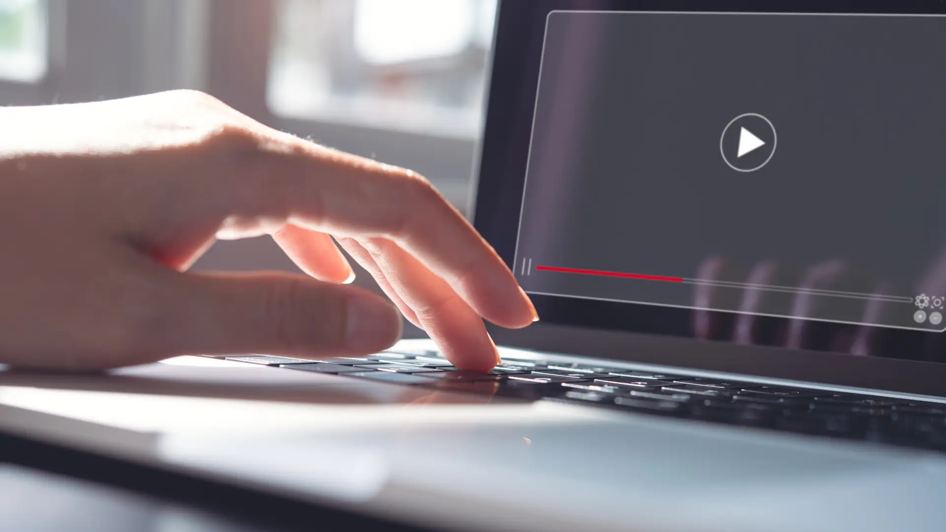 A close up photo of a hand clicking a keyboard. On a laptop screen, there is a grey video box with a play button in the middle.