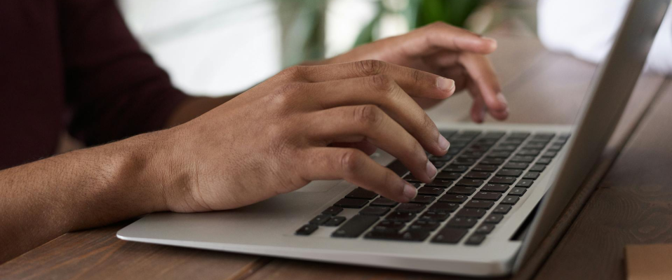 A close-up photo of a man's hands typing on a silver laptop