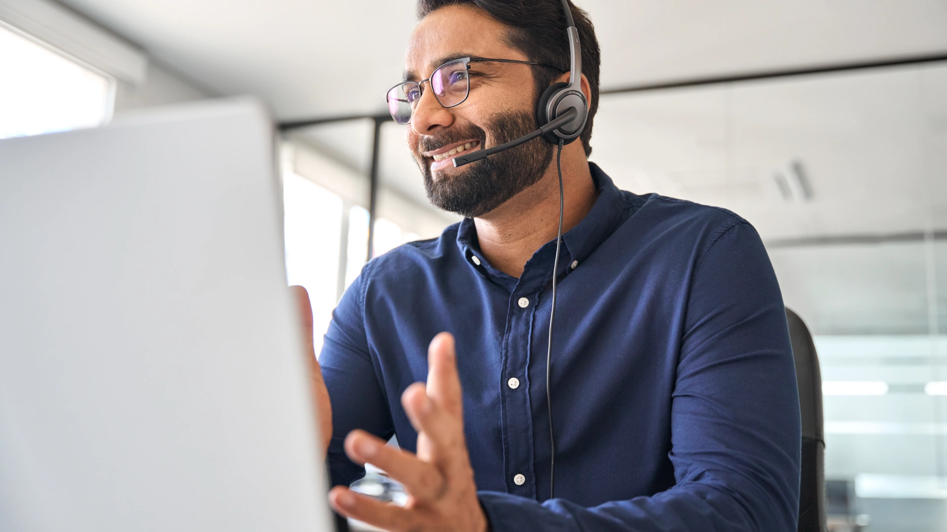 A photo of a man wearing a headset working in the office. There is a computer in front of him.