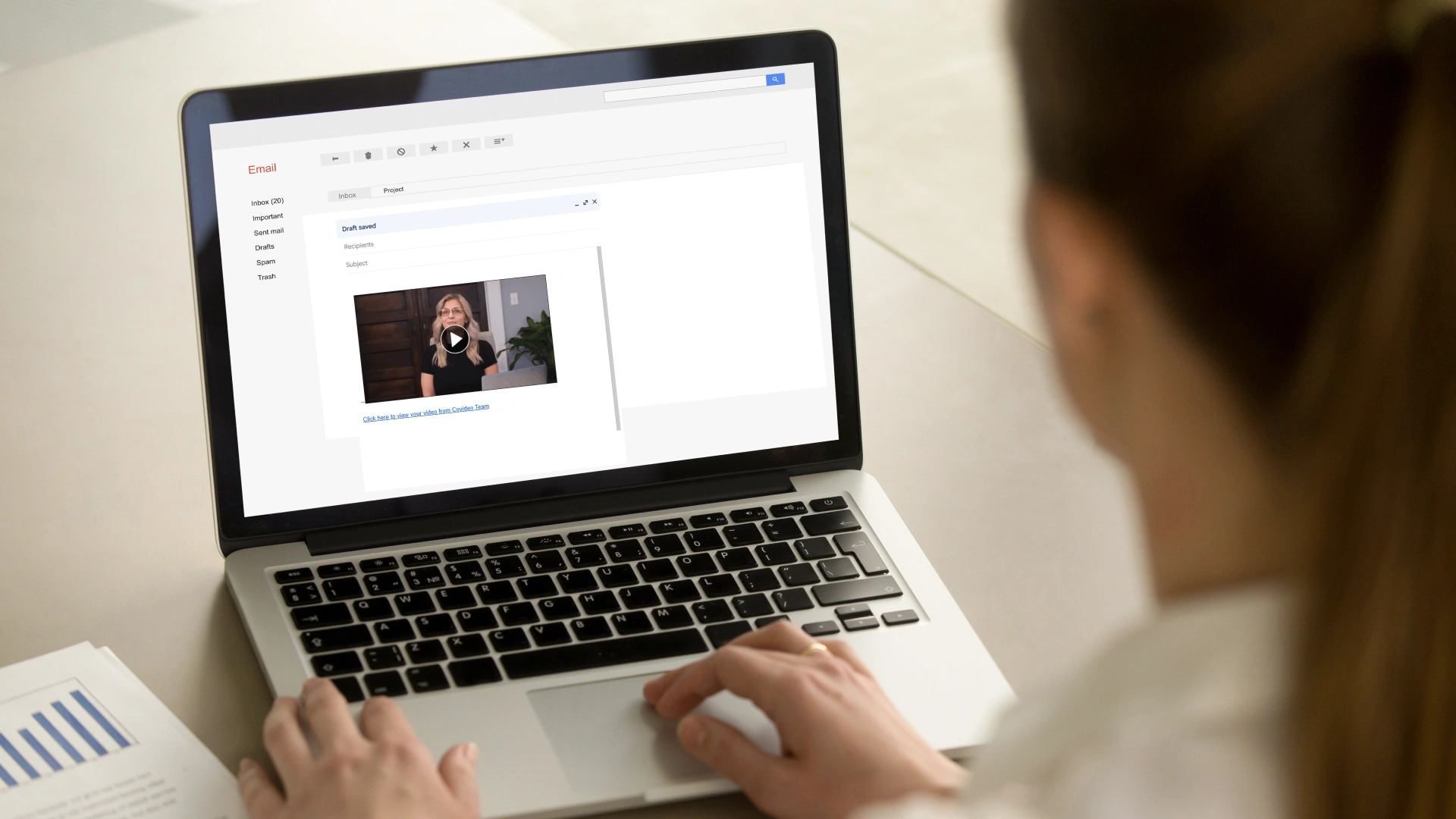A woman works on an emal interface, and you can see a video with a play button inside the email.