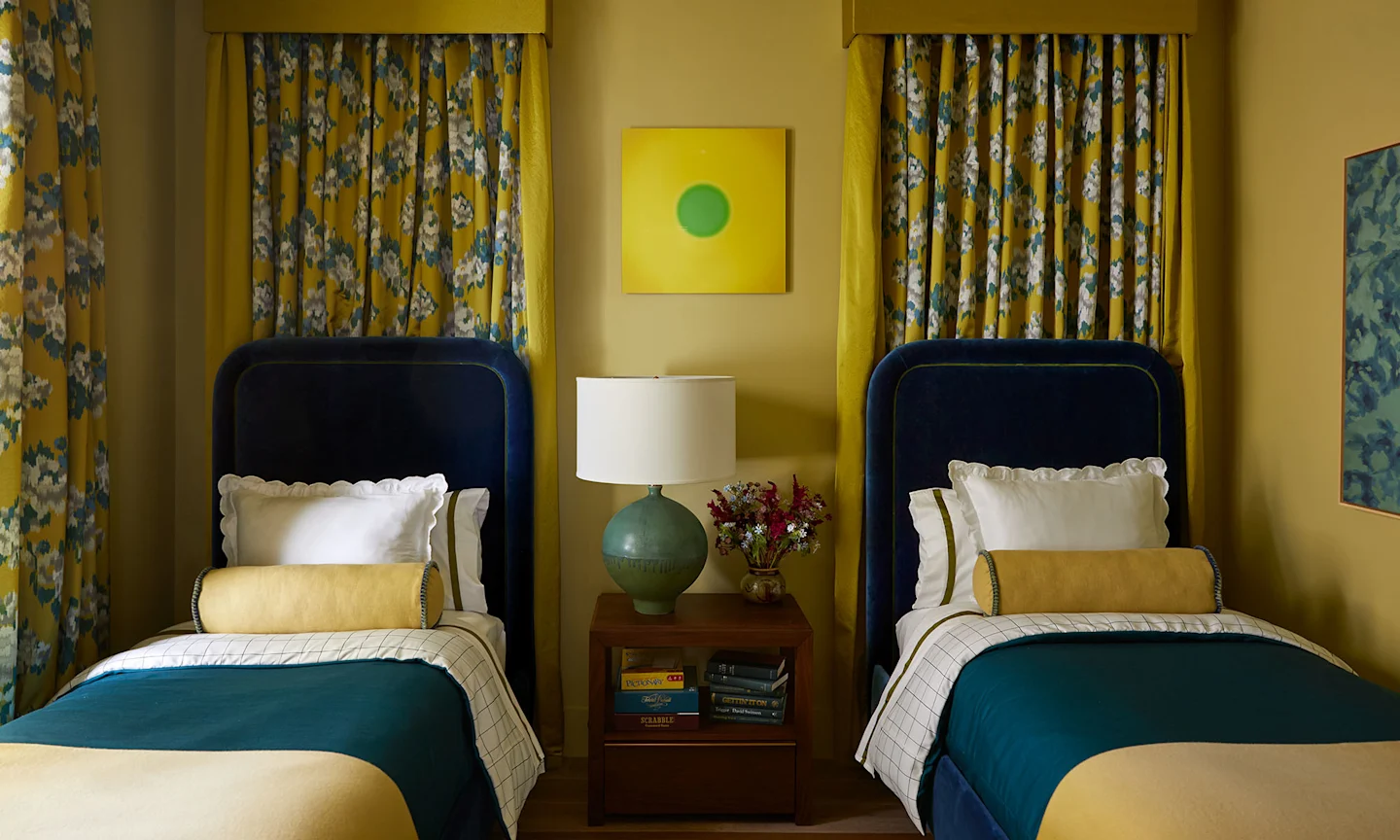 A bedroom with two beds with yellow floral curtains.