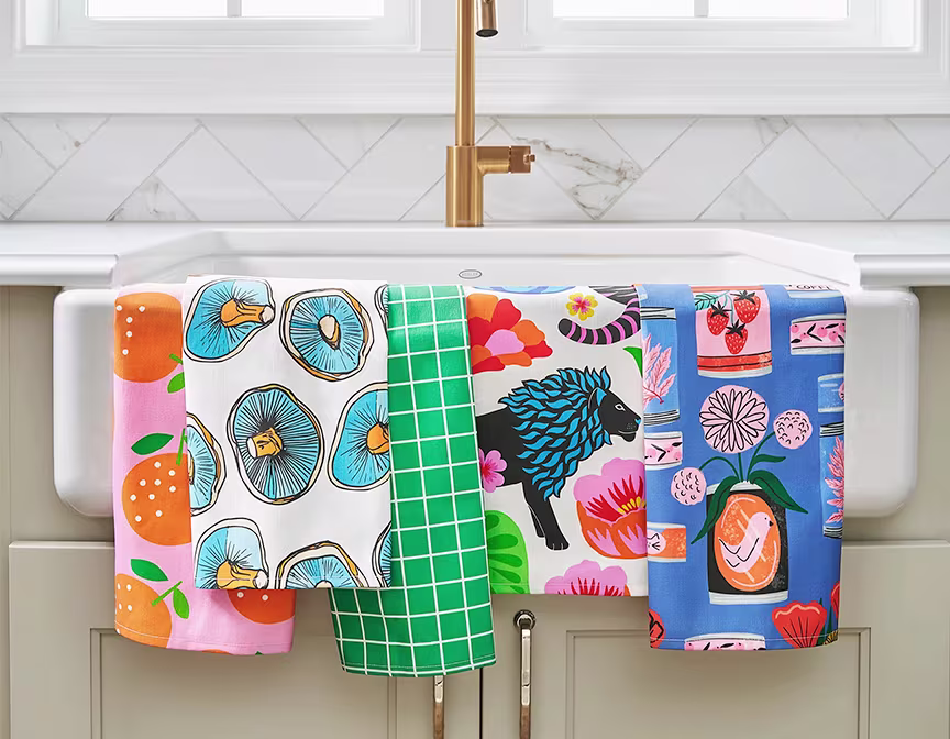Multiple colorful tea towels hanging on kitchen sink.