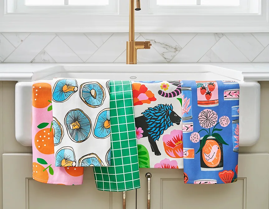 Multiple colorful tea towels hanging on kitchen sink.