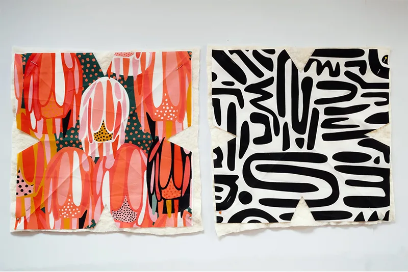 Two cut-out fabric pieces lie next to each other and design side up on a white surface. Each piece has two diagonal creases pressed into it, one going top left to bottom right and one going top right to bottom left, to make an “X” shape. Each square has a