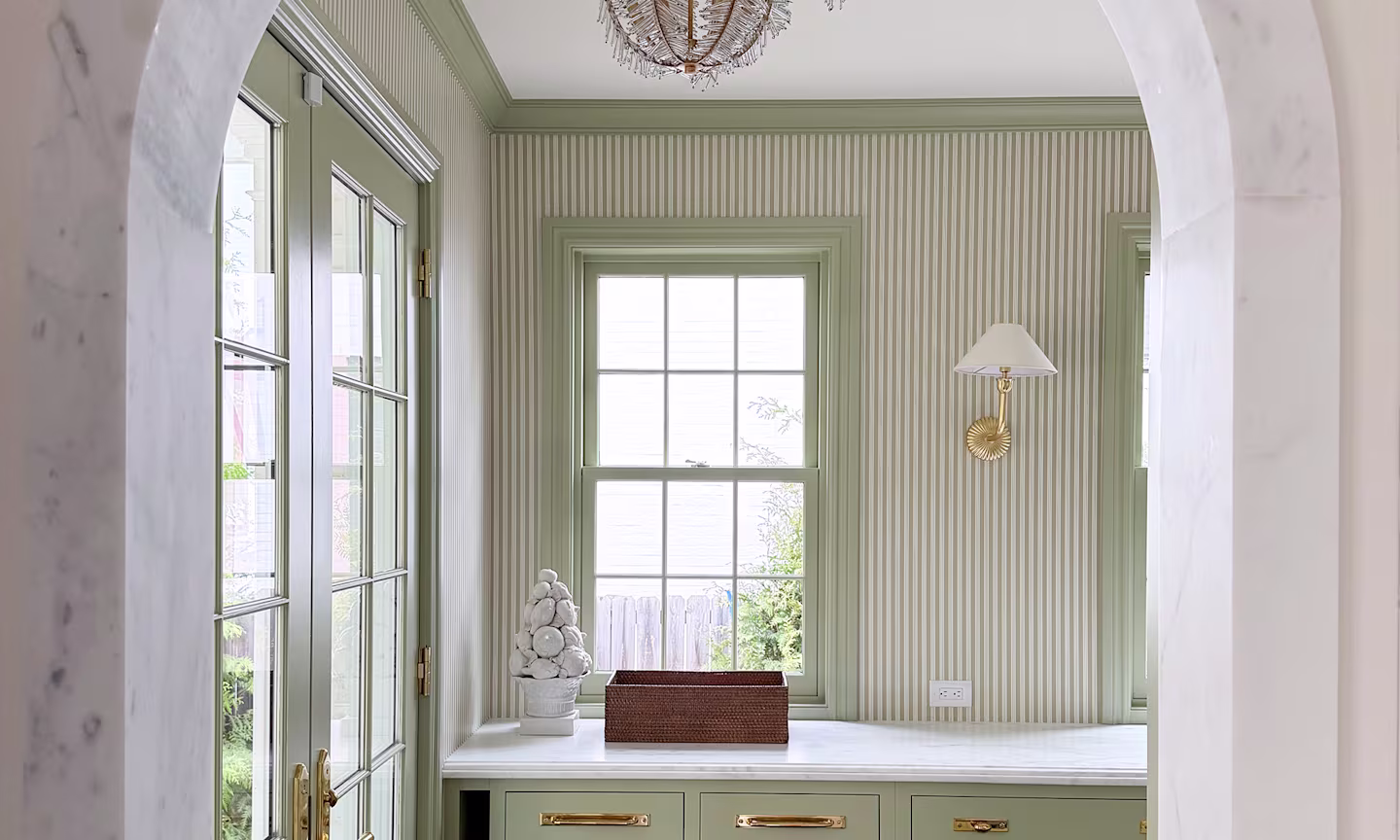 Kitchen with green vertical stripe wallpaper, green cabinetry and trim around windows and brass accents.