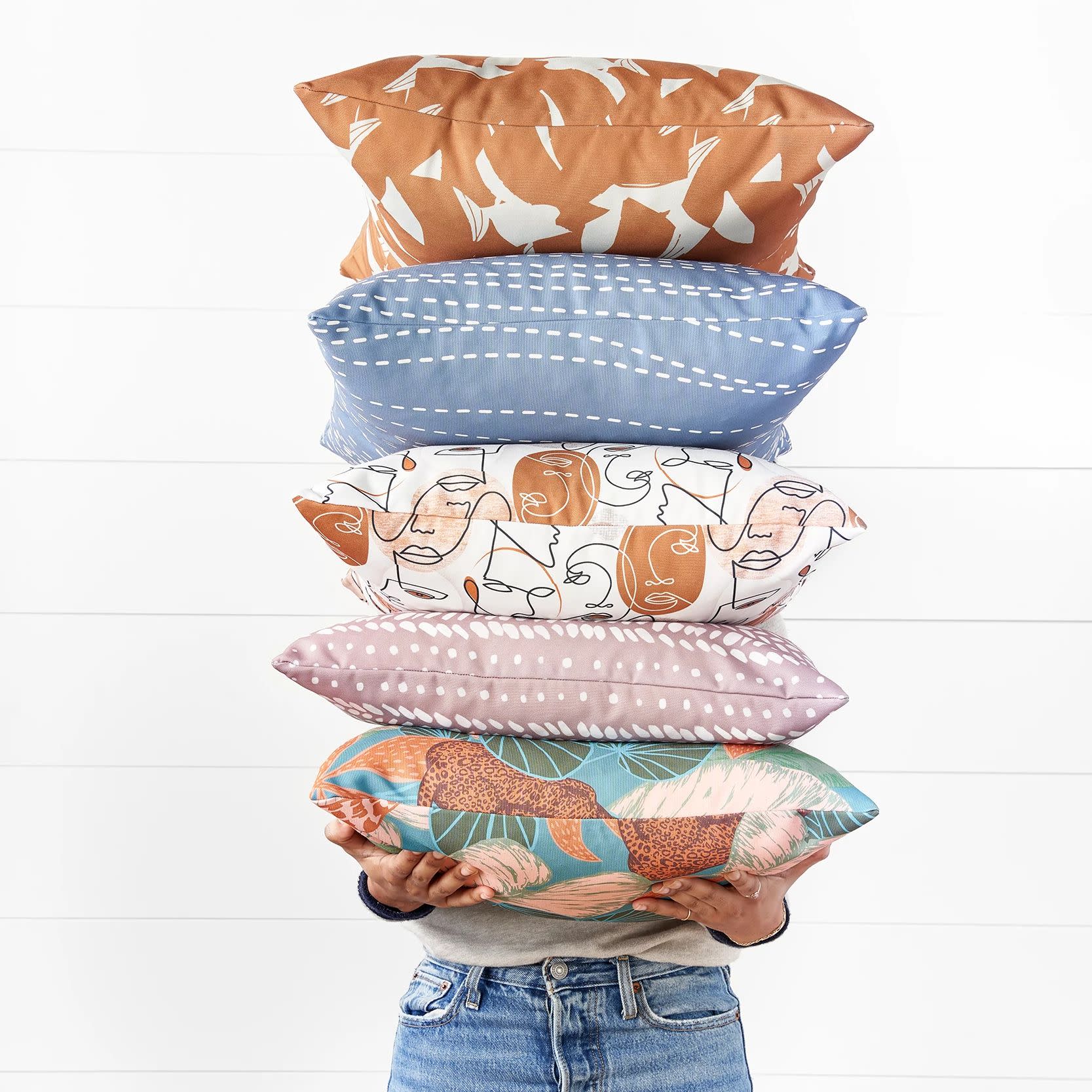 A person holding a stack of square throw pillows
