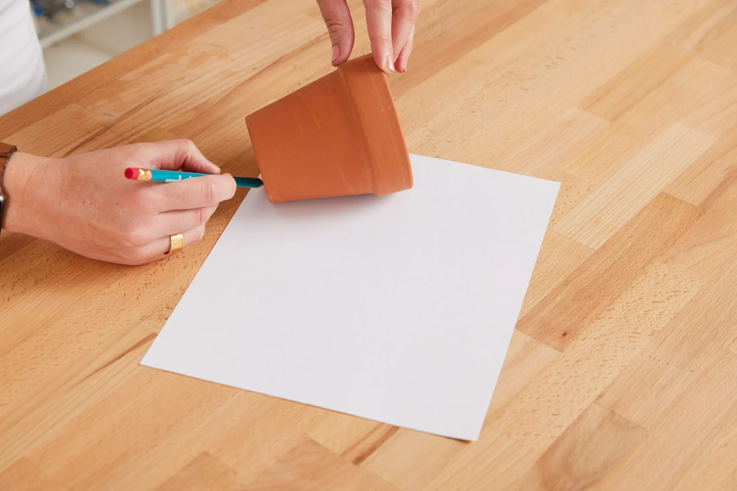 Alexa uses a pencil and a piece of paper to create a paper template for her fabric-covered flower pot. She is just starting the process of drawing the template. The bottom edge of the flower pot is touching the bottom left edge of the piece of paper. The