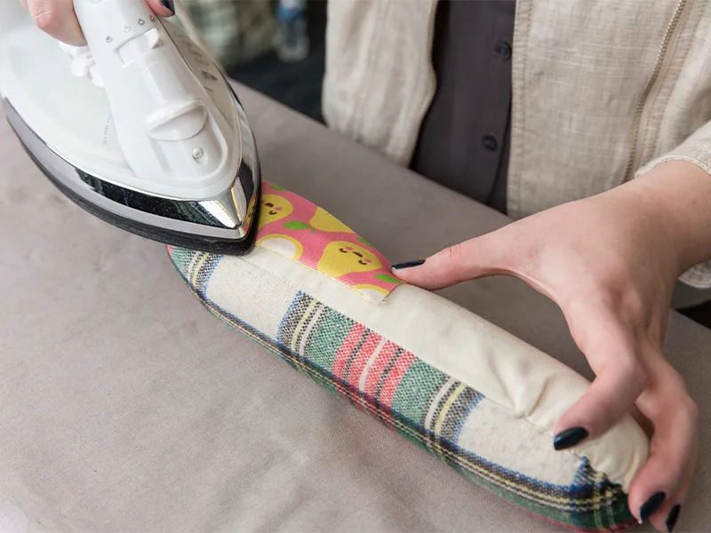 A woman is ironing a folded piece of fabric with an iron and tailor's ham.