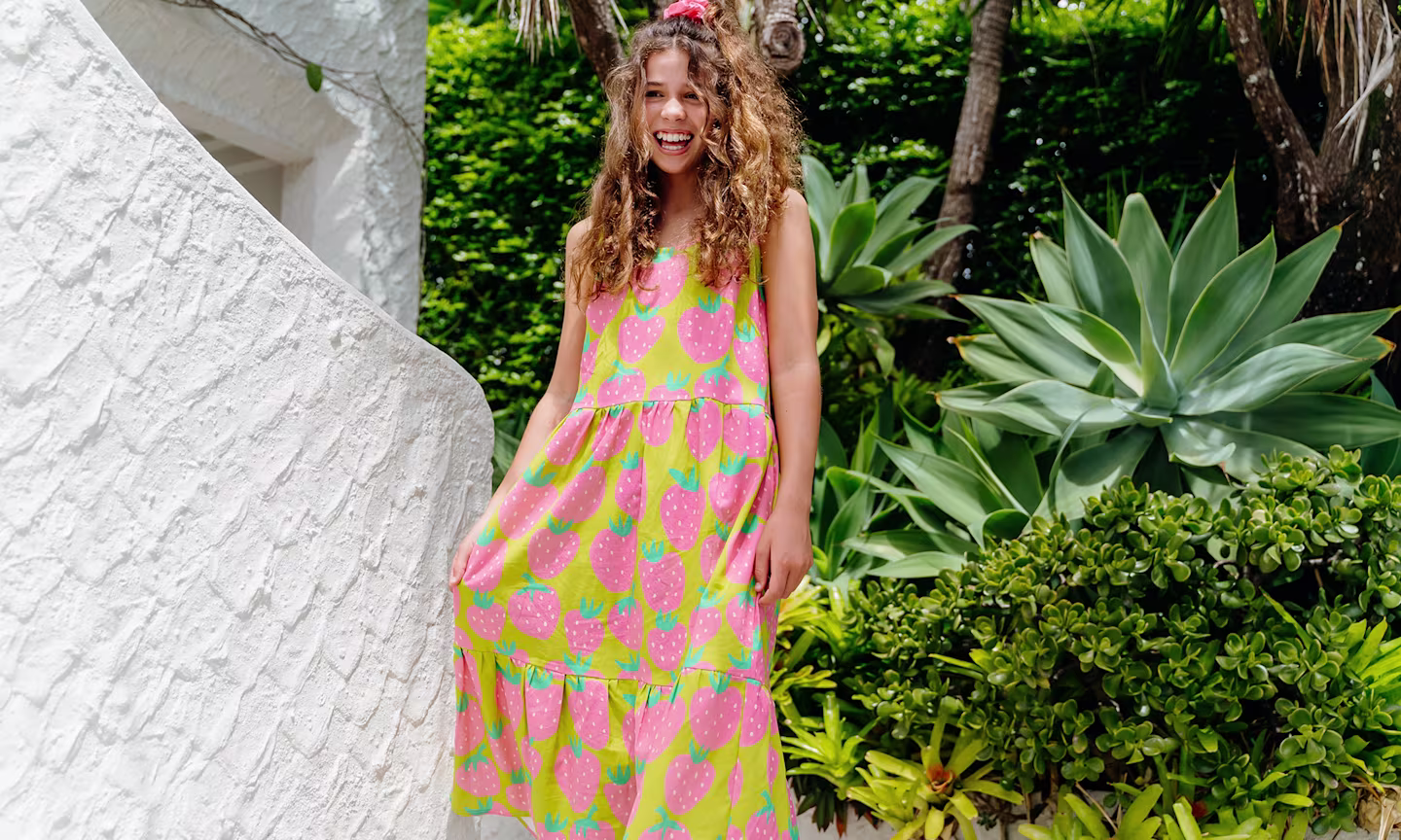 Girl standing outside in a green and pink strawberry dress made of Essex linen.