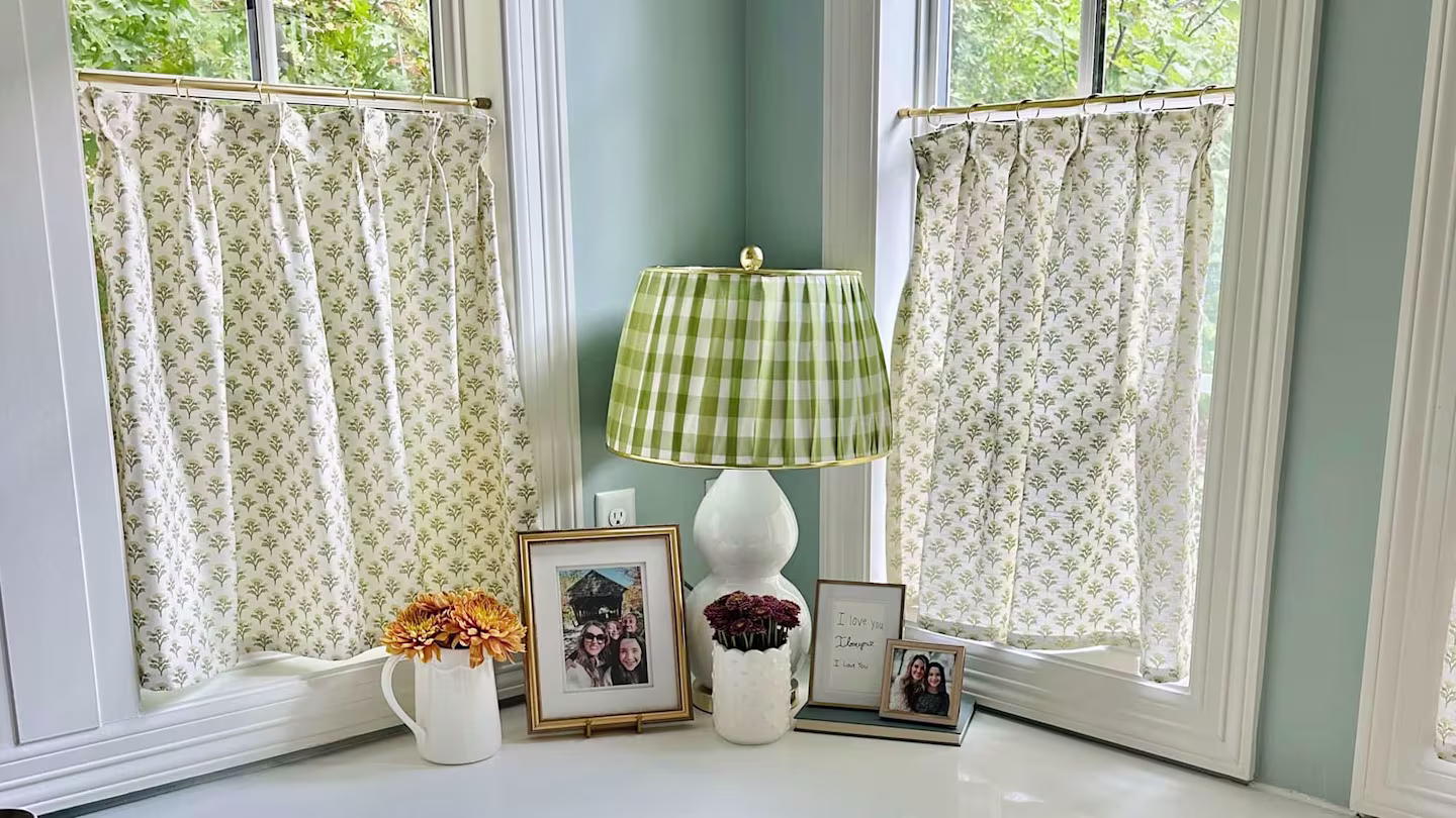 Half curtains in two windows, a white lamp with green plaid and two white vases.