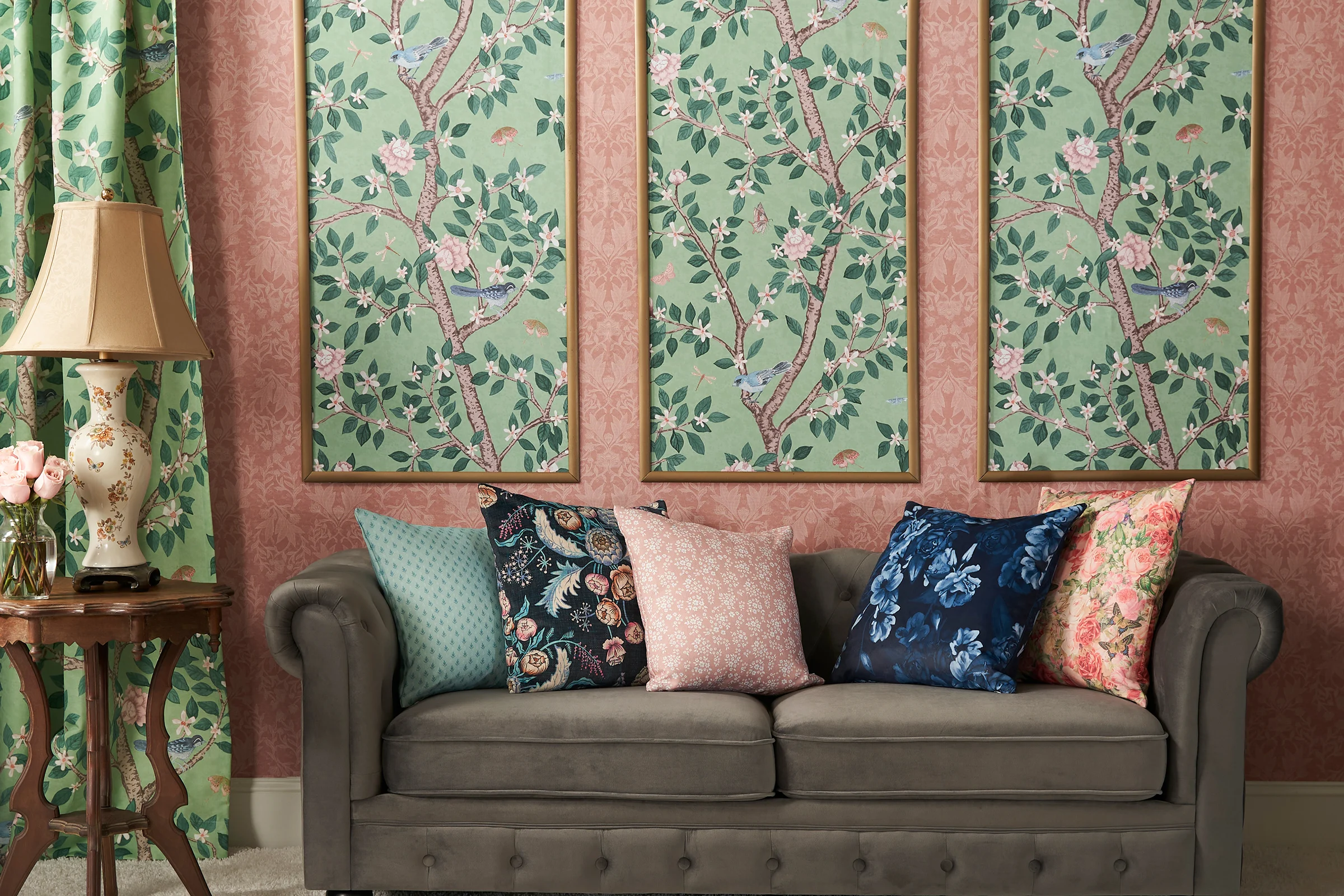 Living area with pink and green floral wallpaper, pillows and curtains.