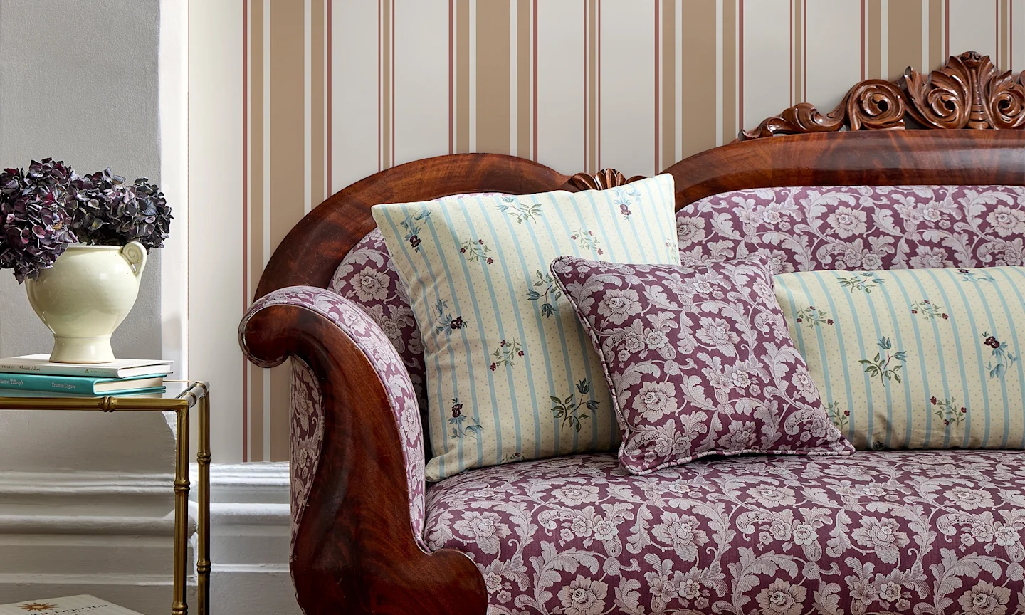 Living area with an upholstered couch, matching throw pillows. and striped wallpaper.