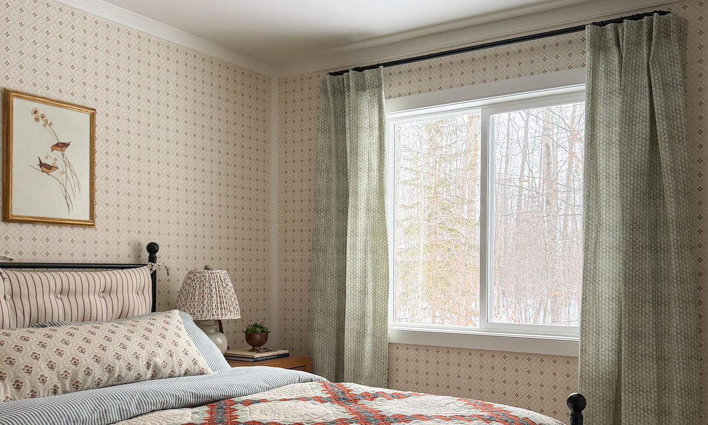 Cabin bedroom with neutral diamond wallpaper, green curtains and coordinating bedding.