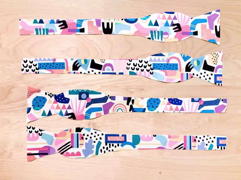 Four pieces of fabric cut for a bowtie lay designs ide up on a wooden surface.