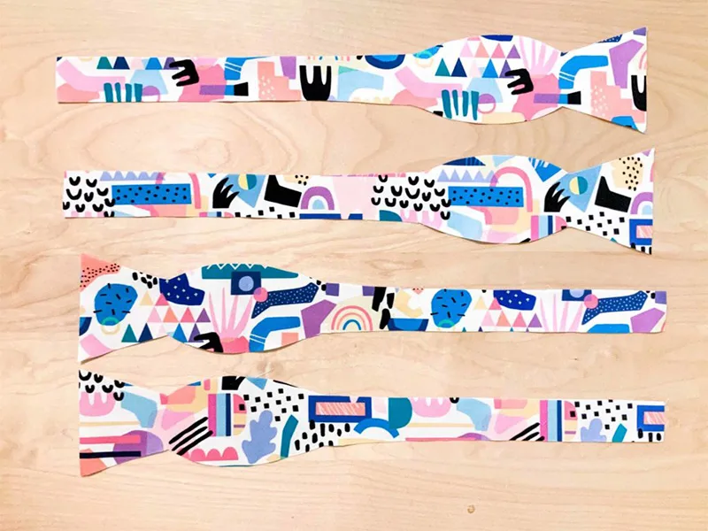 Four pieces of fabric cut for a bowtie lay designs ide up on a wooden surface.