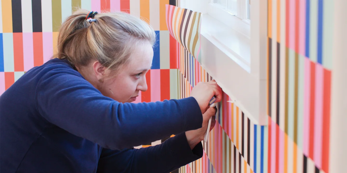 Person trimming peel and stick wallpaper around a window.