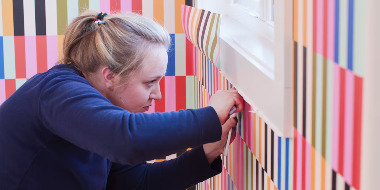 Person trimming peel and stick wallpaper around a window.
