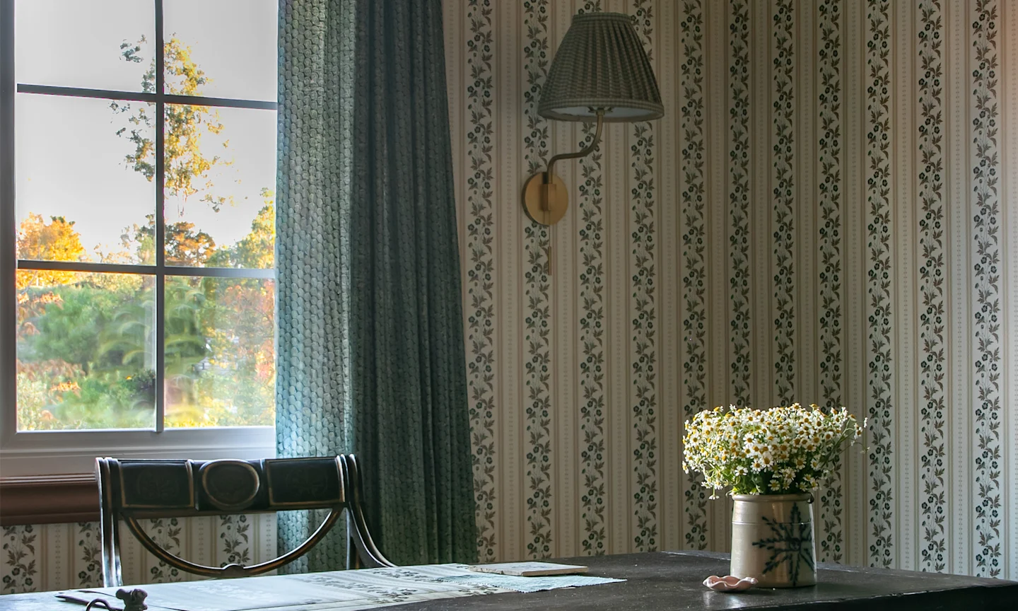Home office with striped floral wallpaper and curtains.