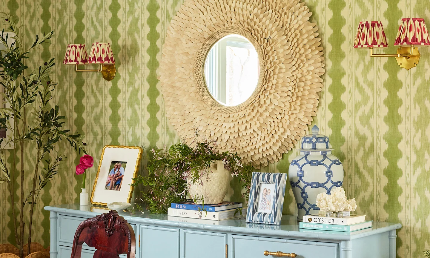Dining room withe green striped wallpaper and a blue console table and circular wall mirror above.