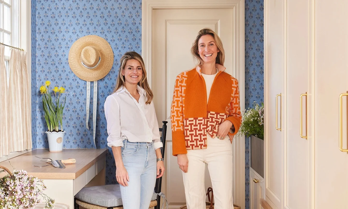 Two women in an entryway with blue wallpaper.