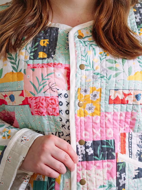 A close up of the front of the snap placket of Meg’s cheater quilt quilted jacket featuring delicate florals, most with a blue or pink theme. She is standing in front of a white wall.
