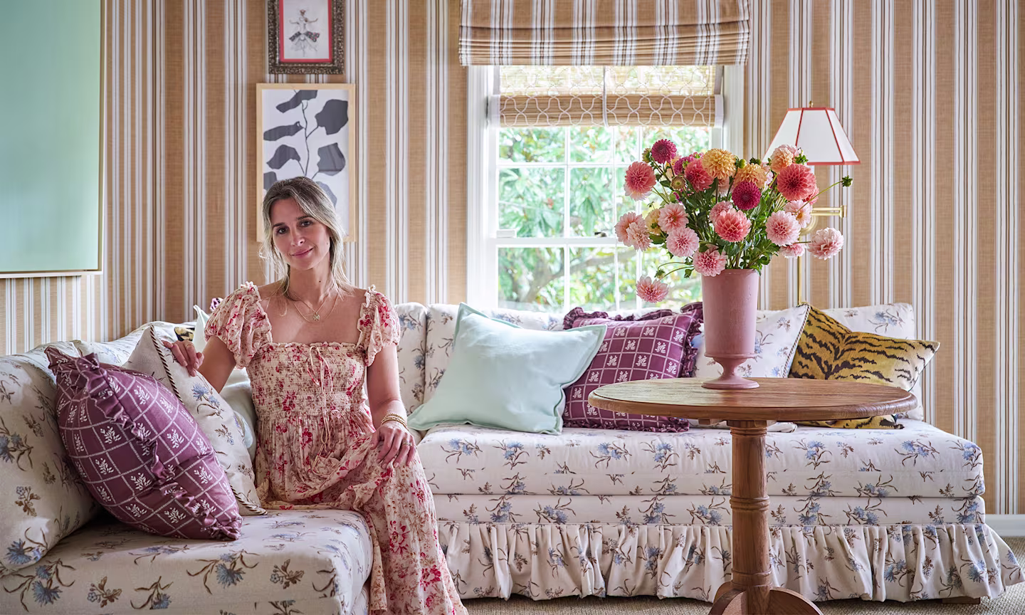 Whiteney McGregor in a living area she designed with striped wallpaper on the walls and a couch upholstered in floral fabric.