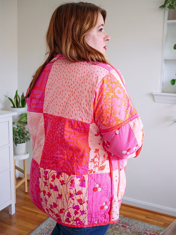 The back and side of Meg’s cheater quilt quilted jacket featuring pink prints and delicate florals. She is standing in front of a white wall.