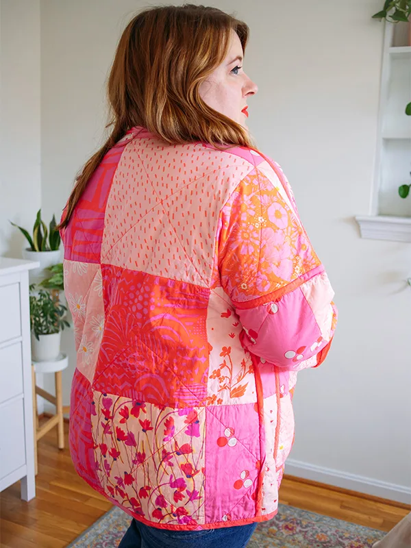 The back and side of Meg’s cheater quilt quilted jacket featuring pink prints and delicate florals. She is standing in front of a white wall.