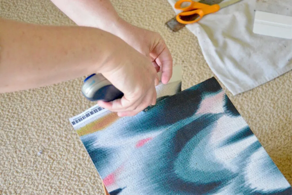 Barb cutting the excess wallpaper from the side of a dresser drawer using a craft knife.