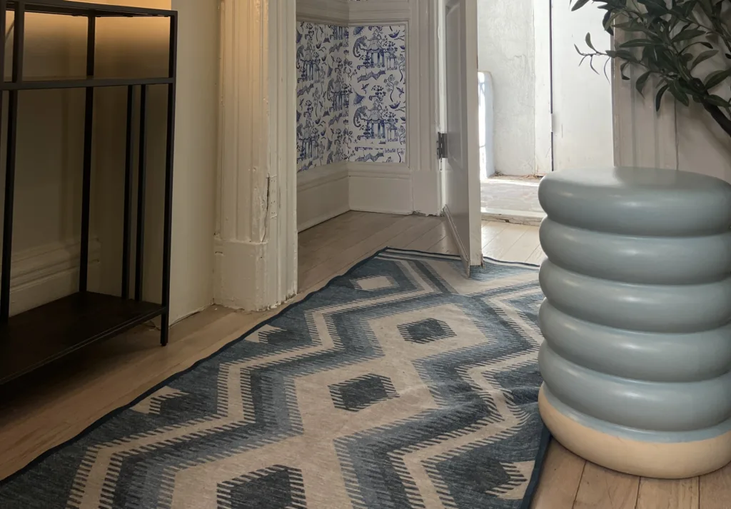 Image of the flooring of a hallway with a light tan wooden floor and a blue-and-white carpet runner.