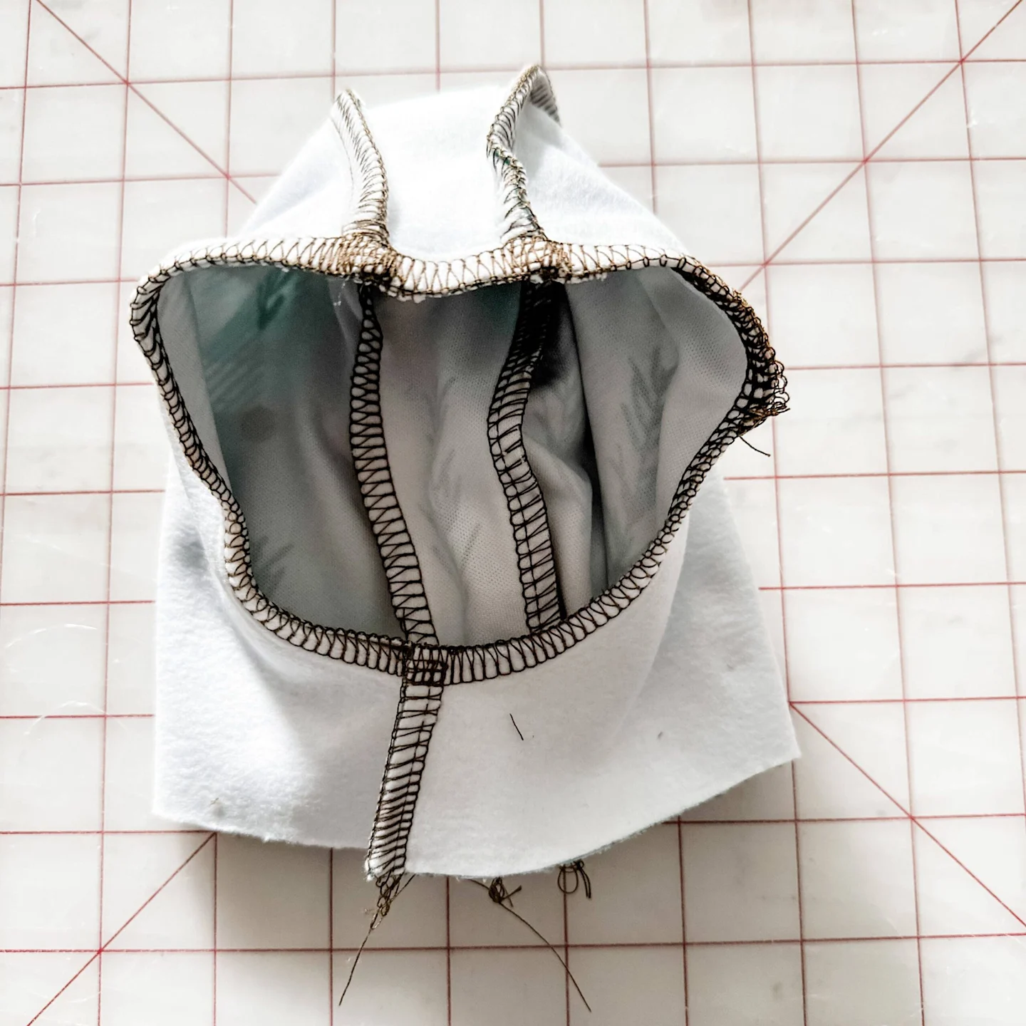 The exterior hoodie piece is turned design side in while the interior hoodie piece is turned design side out, so that the right sides of the fabric are facing each other. The exterior hoodie piece is placed inside the interior hoodie piece. Stitches repla