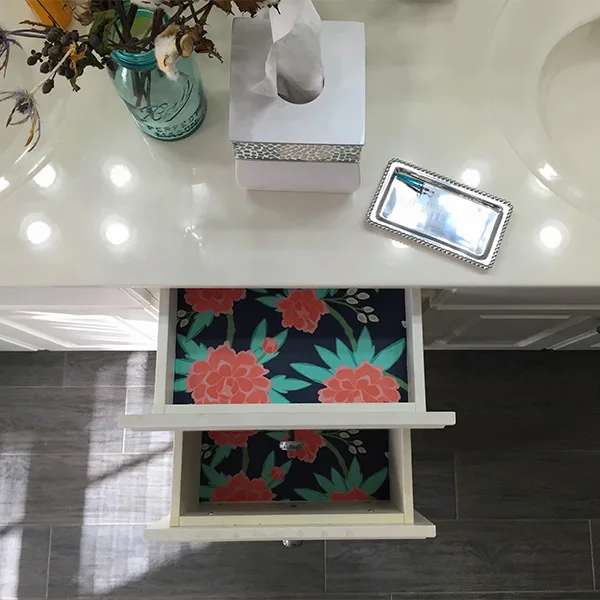 Two drawers in a bathroom are open to expose the new wallpaper lining inside.