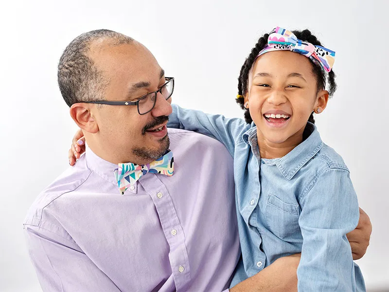 A man wearing a bowtie is looking at a smiling little girl wearing a matching headband.