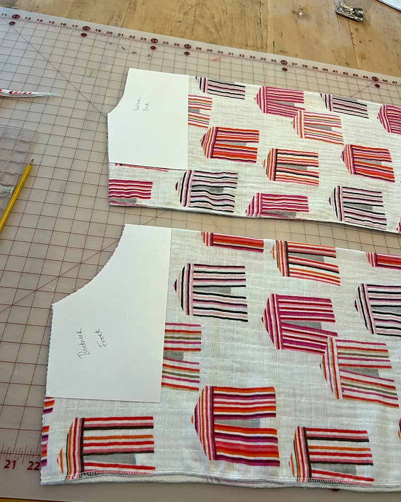 Creating the boatneck front. Two pieces of fabric featuring hot pink cabanas lay on a cutting board.