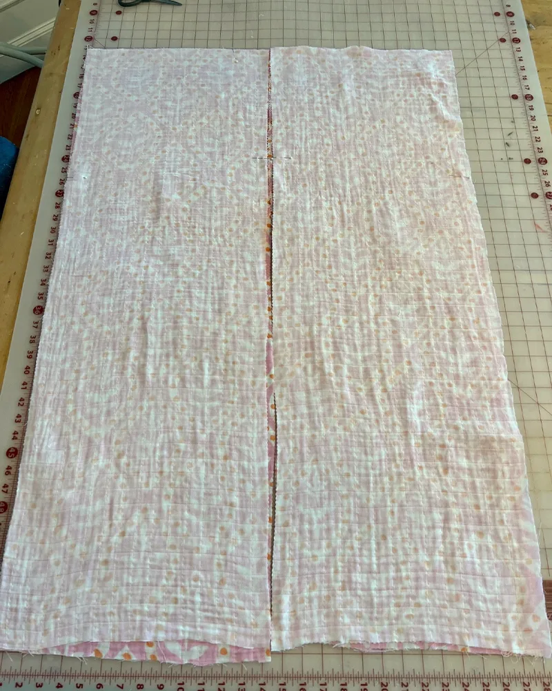 Two stacks of fabric for the V-neck style caftan are laid out with the wrong side facing on a cutting table