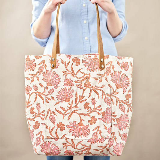 Person holding a large printed tote bag with pocket and leather straps.