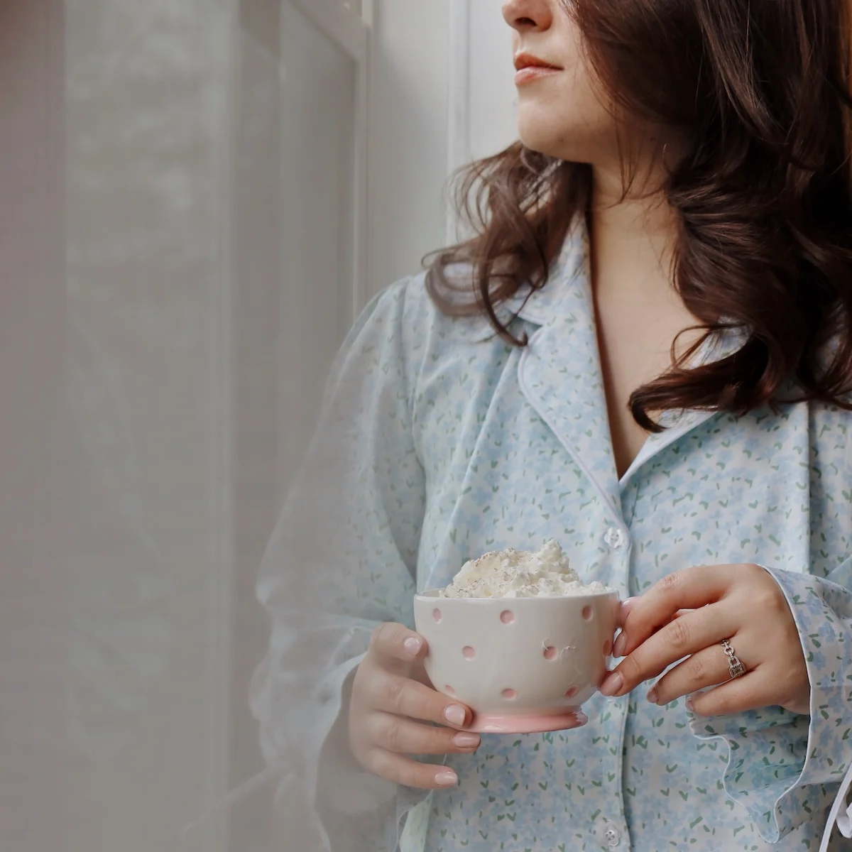 a woman holding a coffee cup, wearing a set of floral pajamas. 