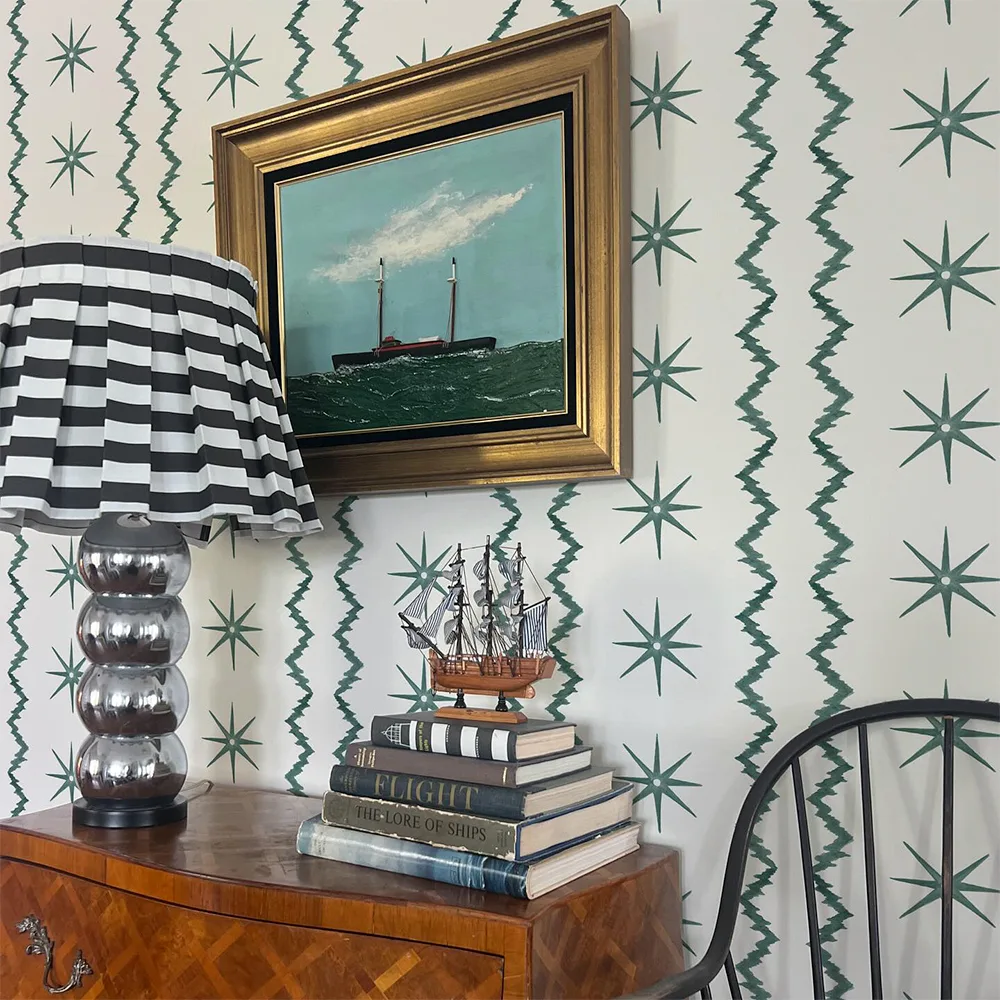 Coastal art and side table in front of a wallpapered wall.