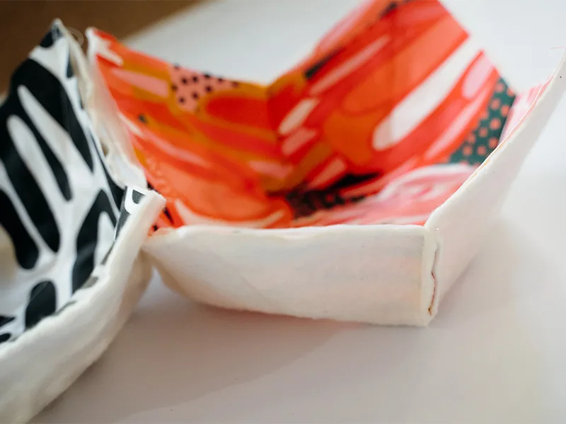 A close up of one of the darts on the side of the bowl cozy. The fabric to the left features bright flowers in pinks, reds, yellows and white. The fabric to the right features black geometric lines on a white background.