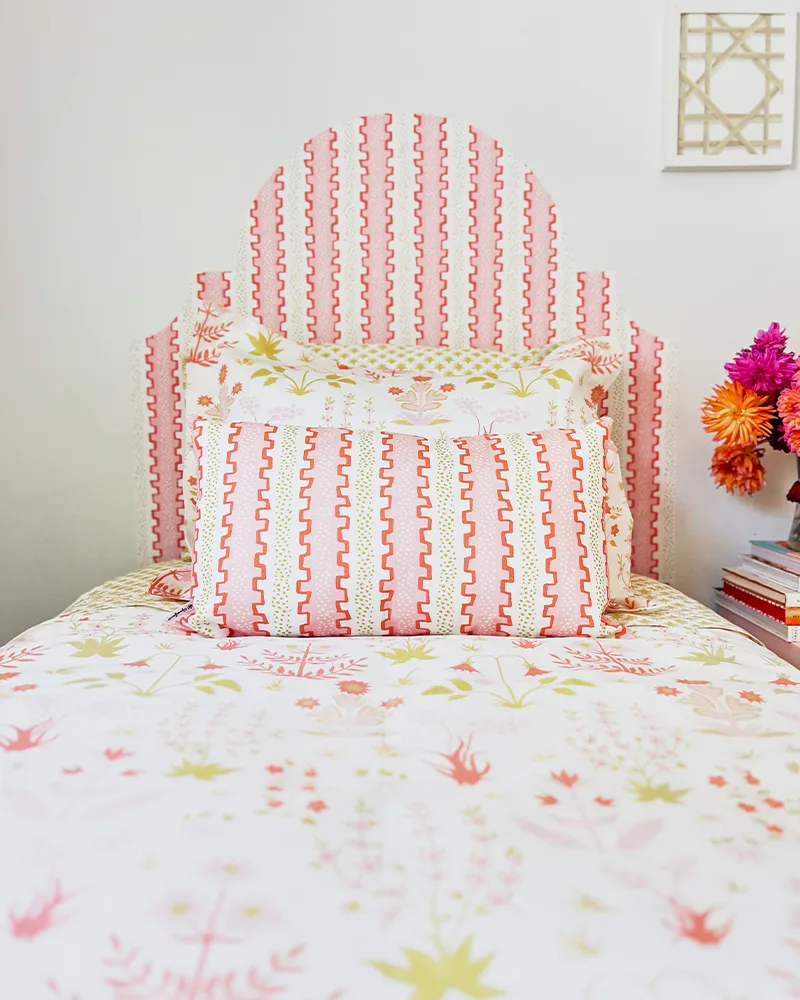A look at the finished headboard and the top of the made-up bed, along with a piece of artwork to the top right, as seen from the bottom of the bed. The designs on the art, bedding and headboard are light pink and green florals.